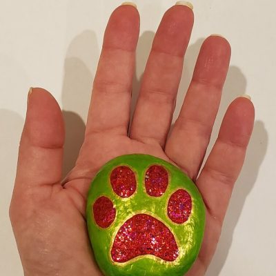 hand holding a painted rock of red dog paw on green background