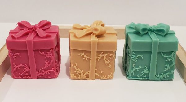 red gold and green goat milk soap in the shape of a one inch cube wrapped present with a bow