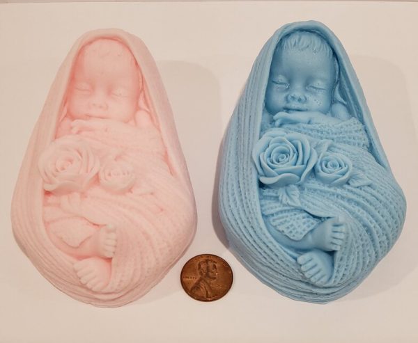 goat milk soap shaped like a baby girl in pink, and baby boy in blue, next to a penny for scale