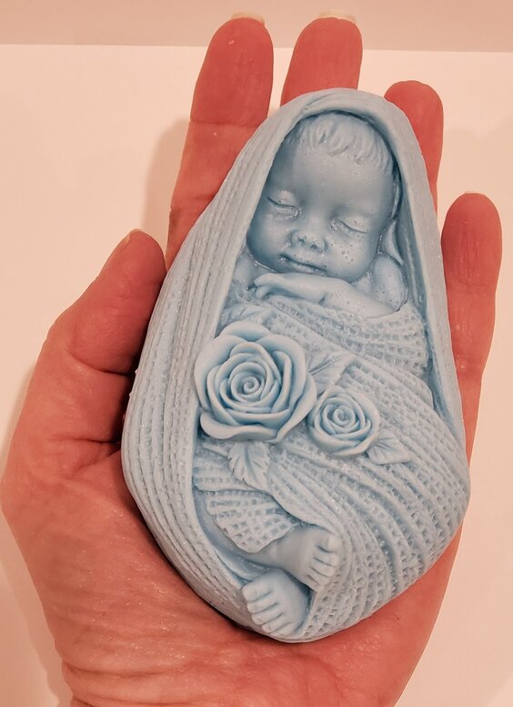 goat milk soap shaped like a baby boy in blue, in a hand for scale